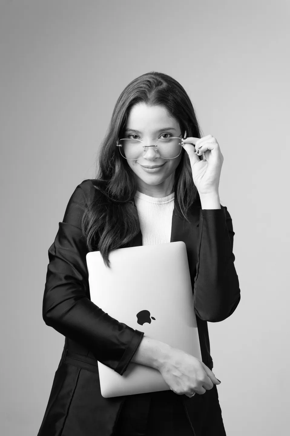 Amanda Tallya de blazer preto, ajustando os óculos e segurando um notebook