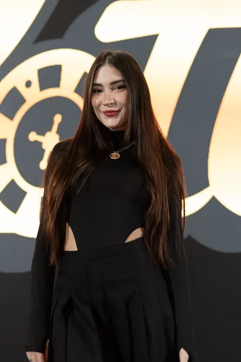 Mulher de preto posando em frente a um painel dourado