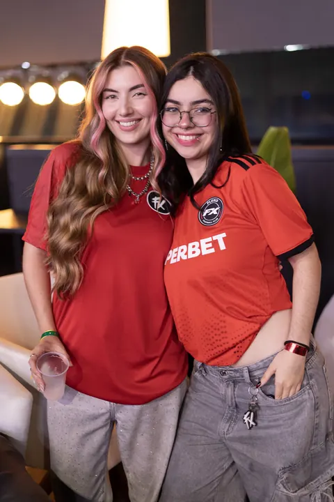 Duas criadoras de conteúdo com camisas vermelhas de time